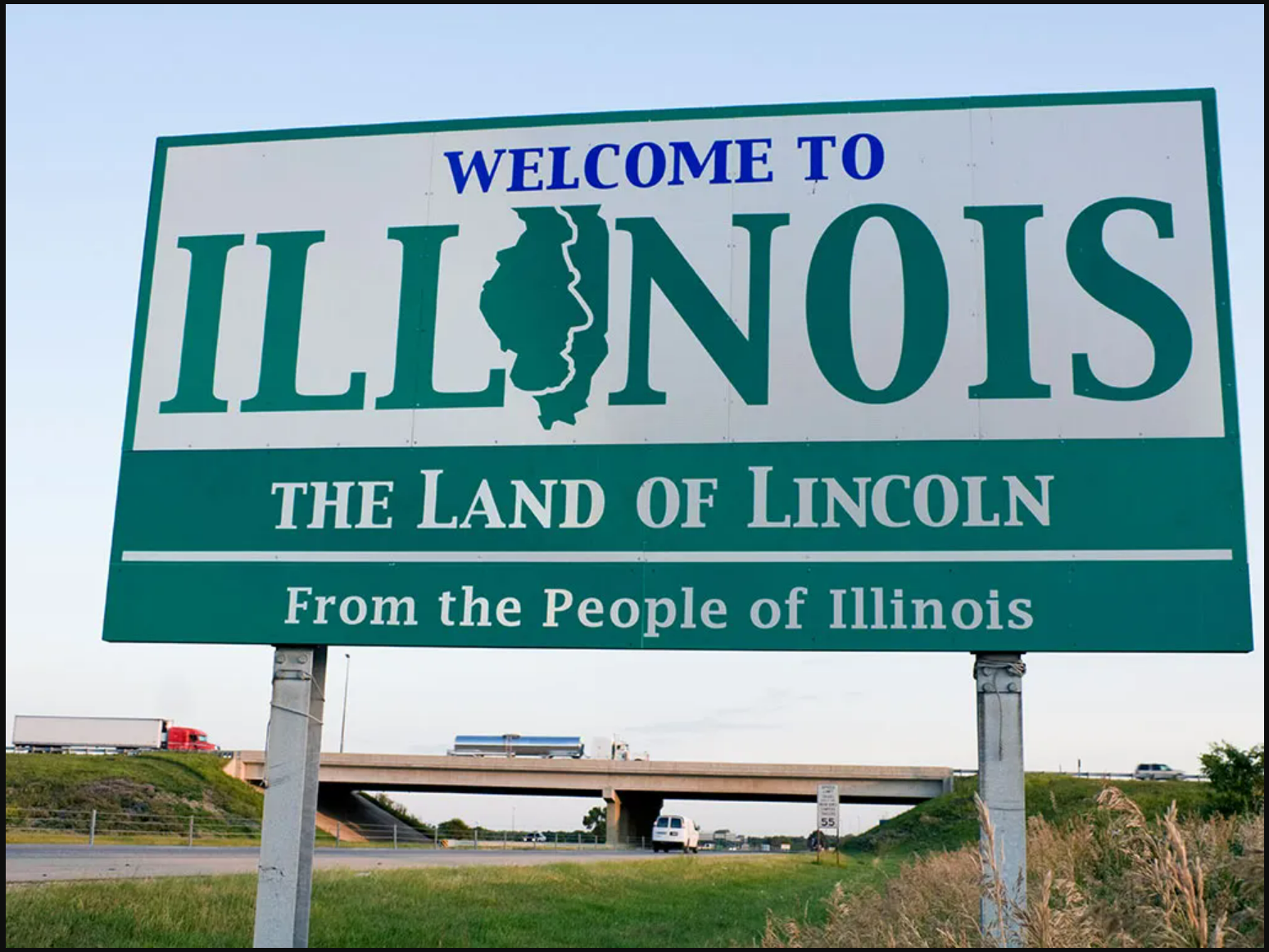 A welcome sign "Welcome to Illinois. The Land of Lincoln" with the highway in the background