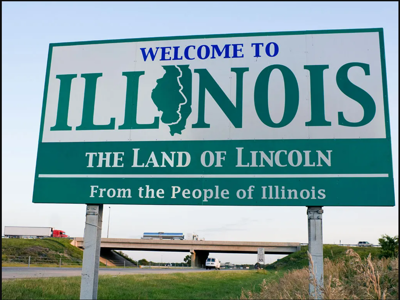 A welcome sign "Welcome to Illinois. The Land of Lincoln" with the highway in the background