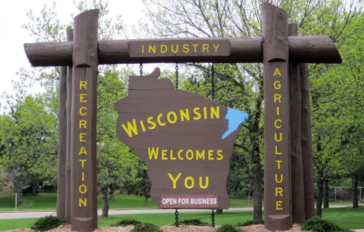 Welcome sign that says Wisconsin welcomes you, open for business. Park in the background