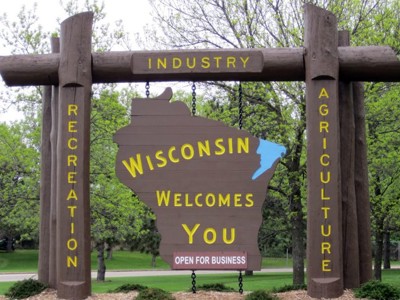 Welcome sign that says Wisconsin welcomes you, open for business. Park in the background